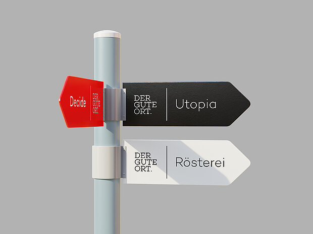 Wegweiser mit drei farbigen Schildern: „Decide“ zeigt nach links, „Utopia“ und „Rösterei“ nach rechts – alle mit dem Schriftzug „DER GUTE ORT“.